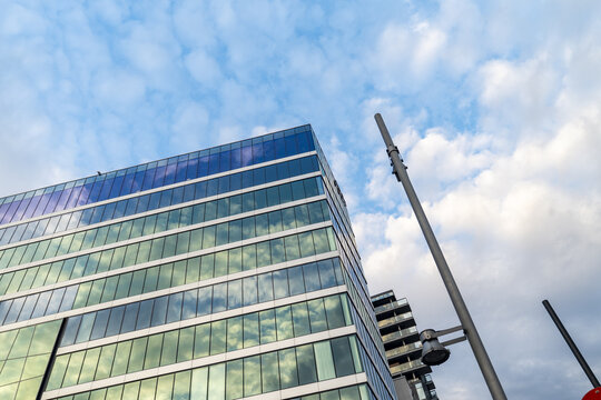 View of a modern glass building reflecting the blue sky and fluffy white clouds, reaching towards the heavens, Oslo, Norway.