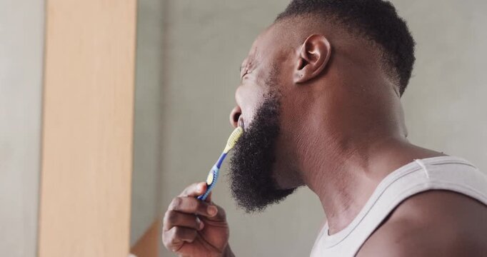 African American man opening mouth lifting toothbrush brushing lower teeth for oral care in sink