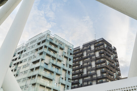 View of modern buildings with contrasting light blue and dark brown facades reach towards a soft, cloudy sky, framed by a white architectural structure, Oslo, Norway.