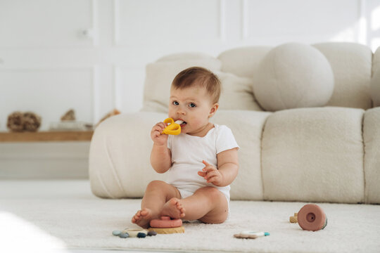 Infant child sitting on soft rug in bright room, playing with colorful toys, plush sofa and wooden decor visible in the background