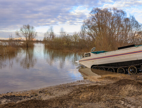 Amphibious vehicle on shore near flooded area with leafless trees