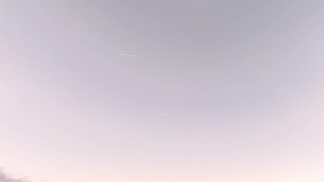 Sunset sky background with soft blue pink violet tones and airplane contrails
