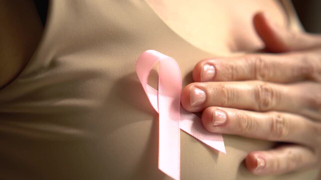 Close-up shot of female hand touching pink breast cancer awareness ribbon on shirt, symbolizing medical support and solidarity in October.