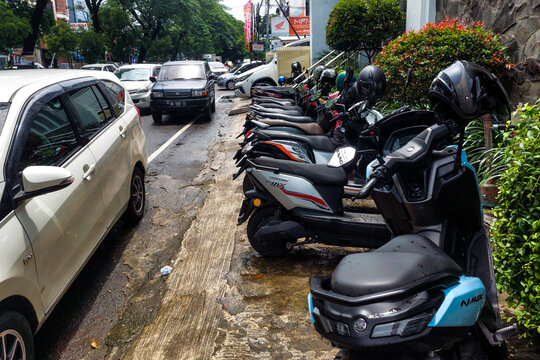 Makassar, Indonesia, December 27, 2025,  Motorcycles and Cars Parked on the Side of the Road