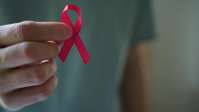 Detailed shot of man's hand giving red awareness ribbon to woman's hand representing united support for HIV positive people.