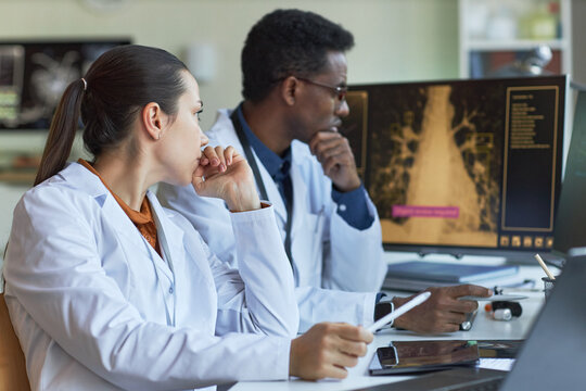 Medium shot of Asian woman and African American man doctors reviewing medical scan on monitor, consulting on diagnosis and treatment planning. Ideal for healthcare teamwork marketing