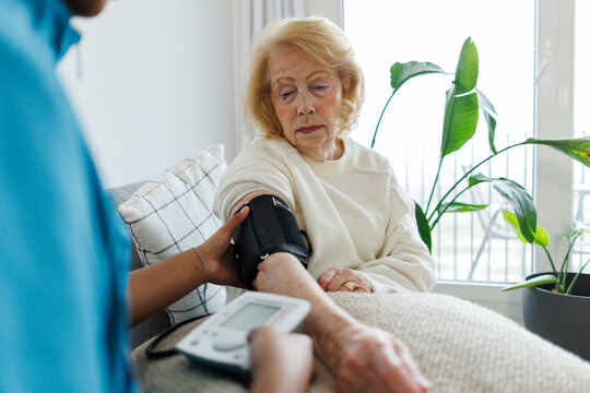 Nurse taking blood pressure checkup of senior at home