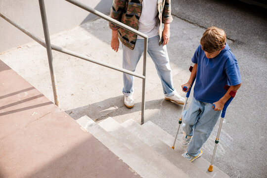 Son using crutches on outdoor stairs with father supporting