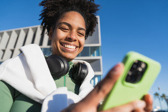 Smiling woman with headphones and smartphone outdoors in urban setting