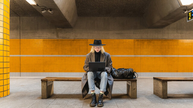 Urban commuter sitting in subway station working on laptop