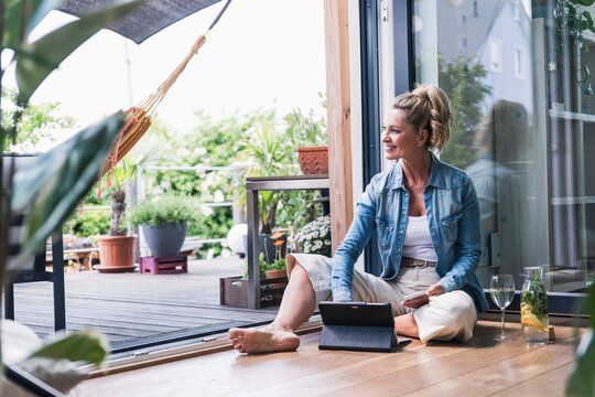 Woman relaxing with tablet and drink on sunny terrace at home