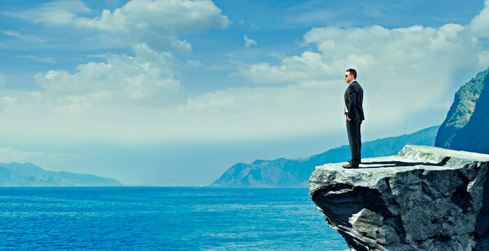 Businessman in suit standing on cliff edge overlooking ocean with vision