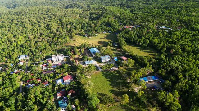 Aerial orbit of rural barangay village settlement amid dense tropical forest during daytime at Guimaras Island, Philippines