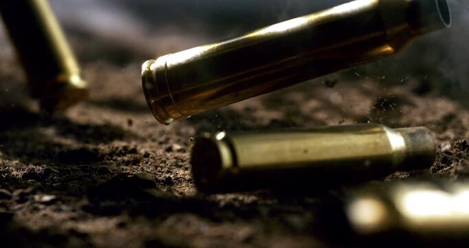 Slow Motion Of Close Up Of Bullet Shells Falling And Hitting Ground With Dust And Impact Particles. Concept Of Violence And War Aftermath. Conflict And After Battle Scene