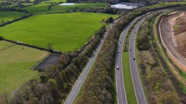 A414 road drone flyover showing a forward approach to a T-junction with traffic, fields and woodland verges. Panshanger quarry visible to the right in Hertfordshire, England.