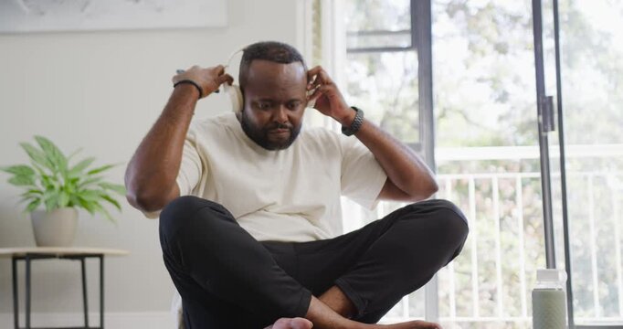 African American man noticing phone alert, putting on headset and scrolling phone near balcony door