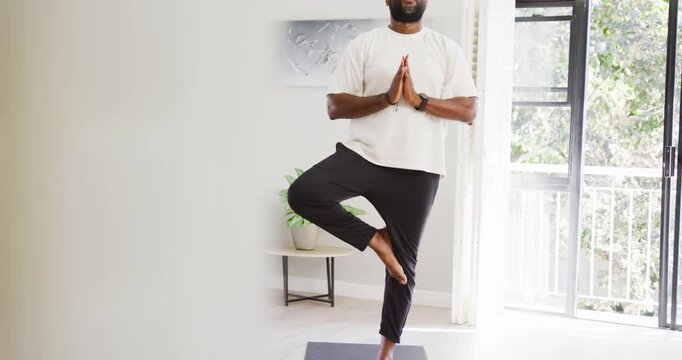 Foreground clearing African American man practicing tree pose at home for balance on black mat