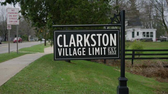 Dolly shot of the Clarkston Michigan village limit sign beside a roadside in daylight