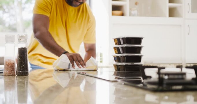 African American man wiping stone kitchen counter with white cloth, preparing for meal containers