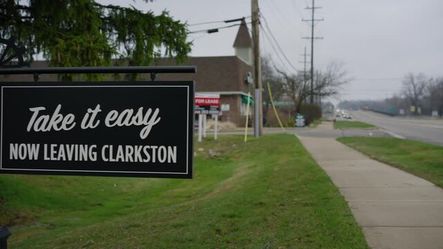 Roadside shot of the Clarkston Michigan village limit sign with take it easy when leaving message in daylight