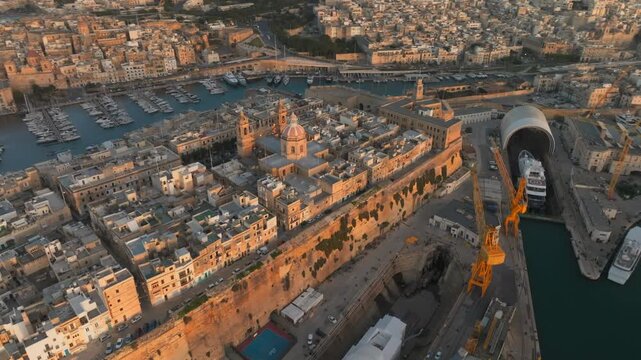 Stunning drone overview of the Three Cities, Senglea, and the Grand Harbour in Malta during golden hour. Showcases historic architecture, yacht marinas, and limestone fortifications.