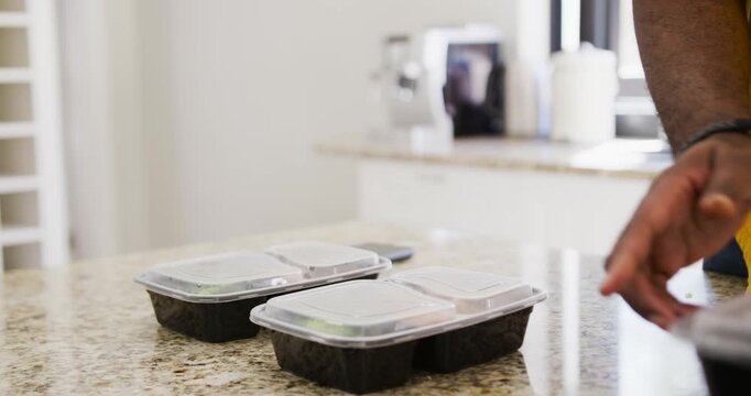 Mid adult African man reaching toward container, stacking meal containers on countertop to store
