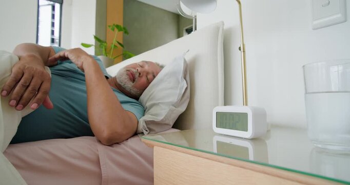 Senior man and woman in bed, alarm clock ringing, man pressing clock to silence, sitting, looking