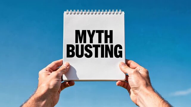 Person holding notebook with myth busting text against clear blue sky background for truth and facts concept