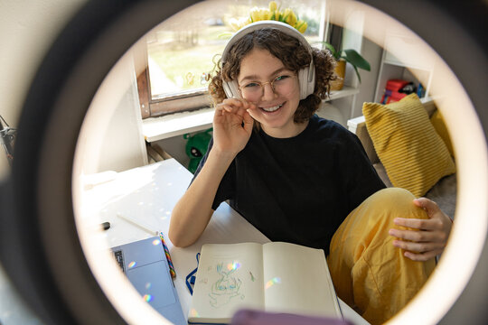 Creative youth with headphones drawing in cozy sunlit bedroom