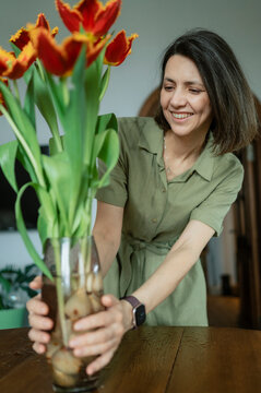 Smiling woman arranging tulip flowers in vase indoors for spring holiday