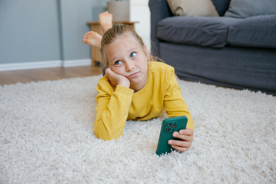 Bored child lying on carpet using smartphone indoors
