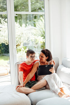 Mother and son sitting on sofa using tablet and sharing trust indoors