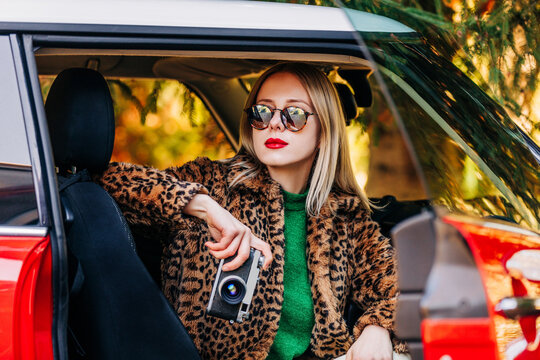 Stylish woman in spotted fur coat with vintage camera in retro car