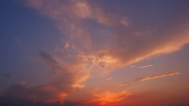 Sunset sky timelapse video featuring cirrus and altocumulus clouds glowing in warm orange and pink hues, drifting across a fading blue horizon, creating a dramatic and atmospheric evening sky scene.
