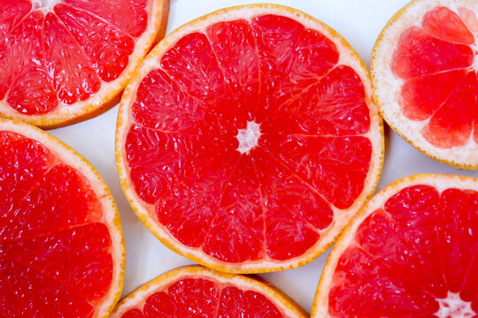 Freshly cut grapefruit slices isolated on a white background, bright pink or red citrus fruit pieces with juicy texture, healthy natural food concept.