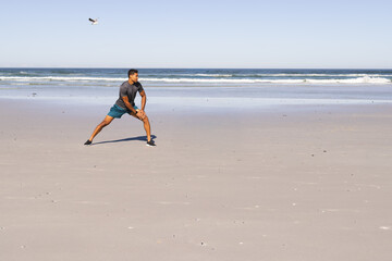 Mid-adult man stretching on sandy beach in shorts and trainers, seagull flying left, copy space © wavebreak3