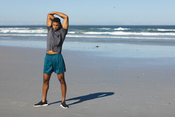 Mid-adult man stretching on wide sandy beach near waterline wearing athletic shirt, shorts, shoes © wavebreak3