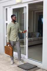 African American man in green shirt holding briefcase, opening sliding glass door at patio to sofa © wavebreak3