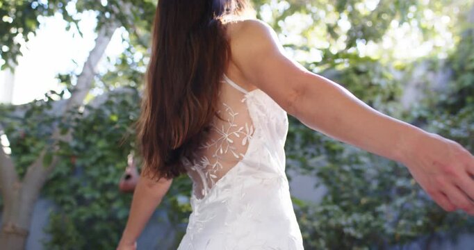 Woman in white sheer back dress raising arms spinning arching turning as sunlight filtering in yard