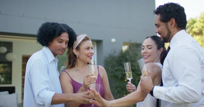 Friends watching man on right showing hand in backyard, leaning in, clinking flutes and celebrating