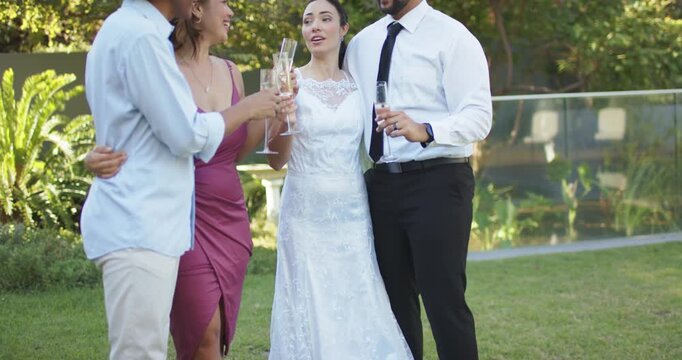 Diverse wedding group celebrating bride in lace gown raising champagne flutes and clinking on lawn