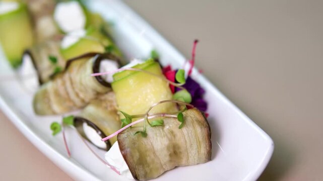 Eggplant and zucchini rolls are served on a long white rectangular plate and drizzled with balsamic glaze.vegetarian appetizer with fresh vegetables and elegant plating in a restaurant style.