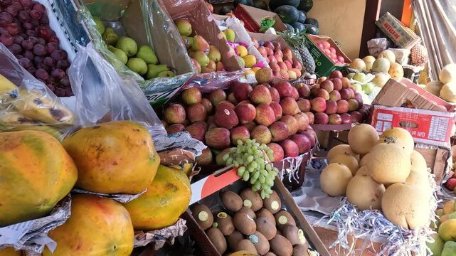 Colorful display of fresh fruits at a local market stall including apples, papaya, grapes, pears, kiwi and melons. Vibrant marketplace scene representing healthy food, organic produce and everyday str