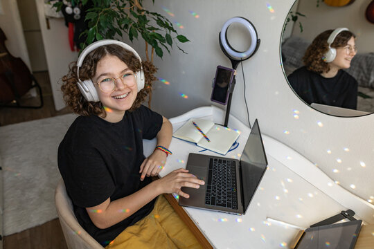 Smiling teenager with headphones studying at desk in cozy bedroom