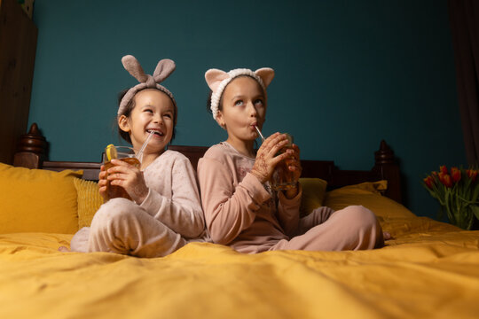 Children in pajamas drinking on bed with bunny ear headbands indoors