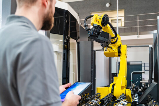 Young man using tablet to control industrial robot in production hall