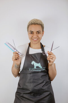 Portrait of smiling groomer holding scissors and comb in salon