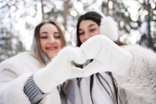 Two friends smiling outdoors in winter forming heart with gloved hands