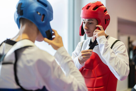 Two martial artists preparing for training with protective gear indoors