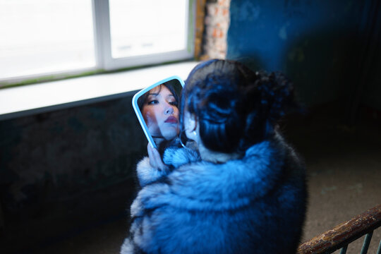 Woman in fur coat looking at reflection in mirror indoors